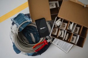 Smartphone mit HERO AI liegt auf einer Kabelrolle zwischen Seitenschneider und einem Karton mit Steckdosen-Einsätzen.